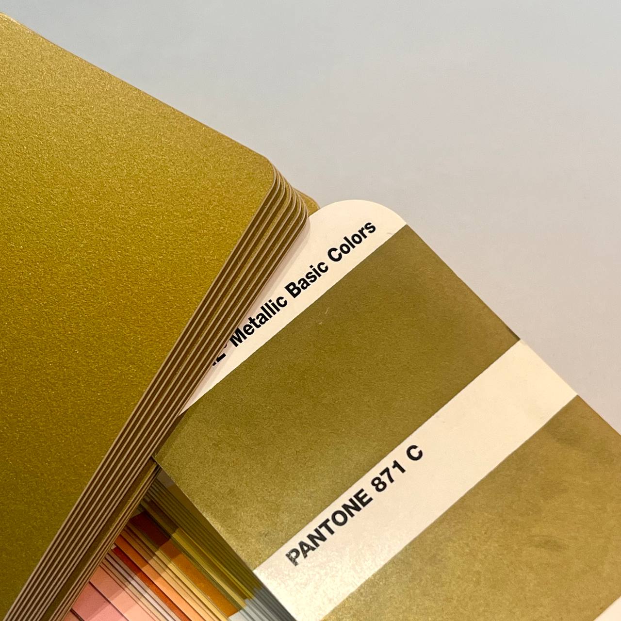 Золотой пластик в массе рядом с веером Pantone Formula Guide. Подбор оттенка при производстве пластиковых карт в типографии МАДЖЕНТА